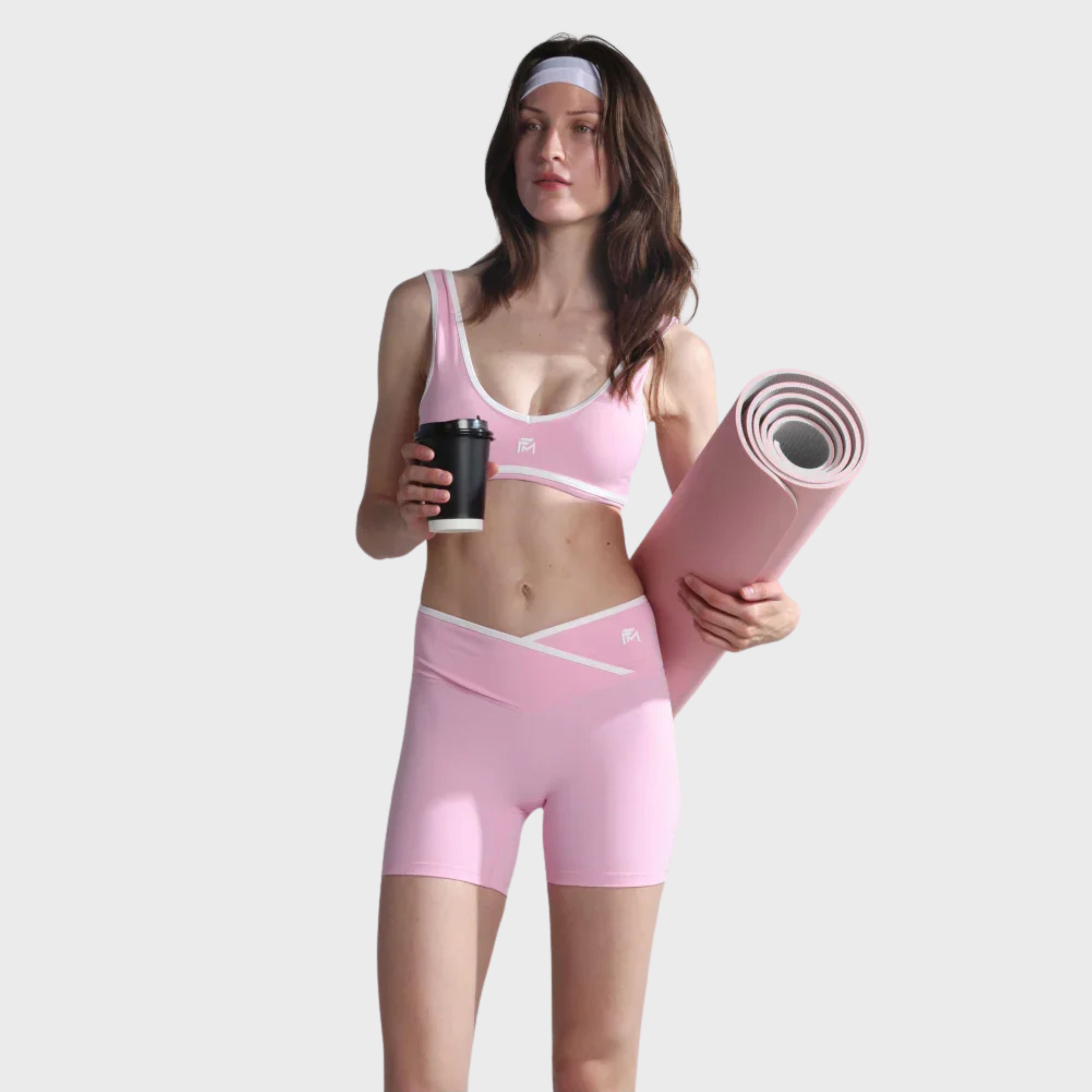 Woman in pink athletic wear holding a coffee cup and yoga mat on a white background