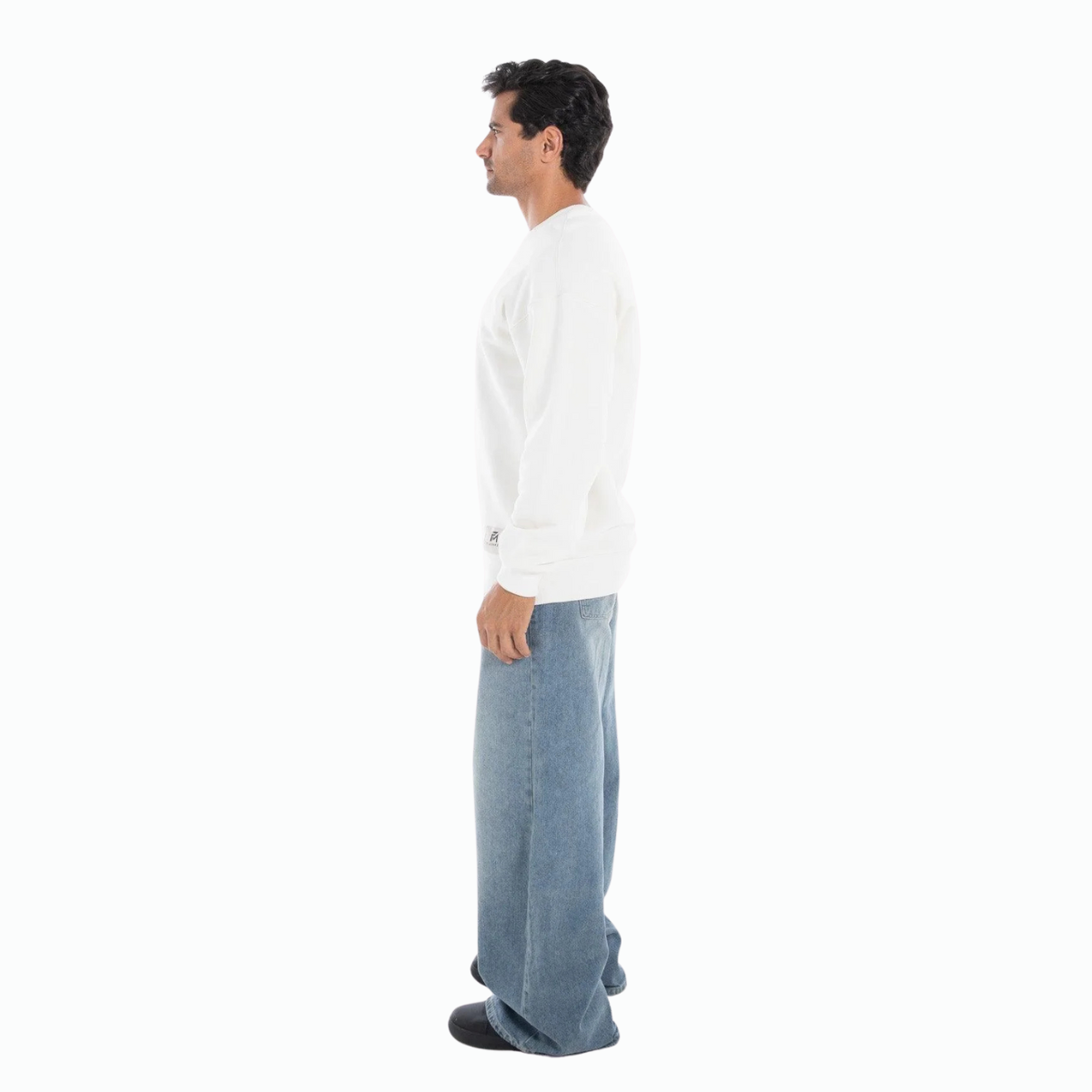 Man wearing white classic crewneck sweatshirt and blue jeans standing in profile on white background