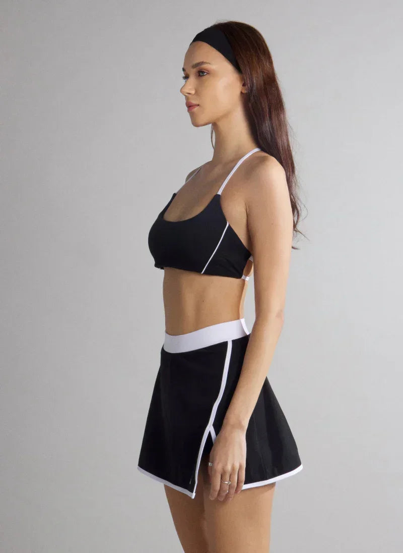 Woman wearing a black sports bra and skirt with white trim on a gray background